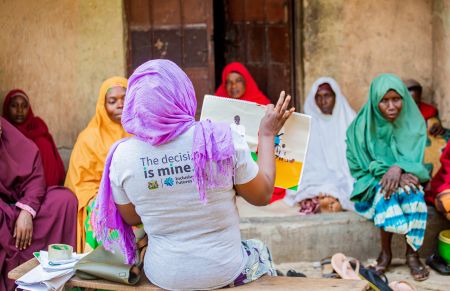 A woman wearing a grey T-shirt with the words 'The decision is mine' leads a workshop with other women with disabilities in a courtyard in northern Nigeria
