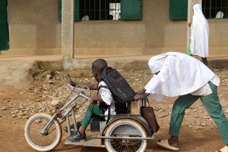 A young girl wearing a school uniform is pushing a young boy, also in school uniform, on a tricycle outside their school in northern Nigeria. 